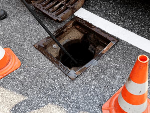 Pozzetto fognario aperto su sede stradale durante un intervento di spurgo fognature