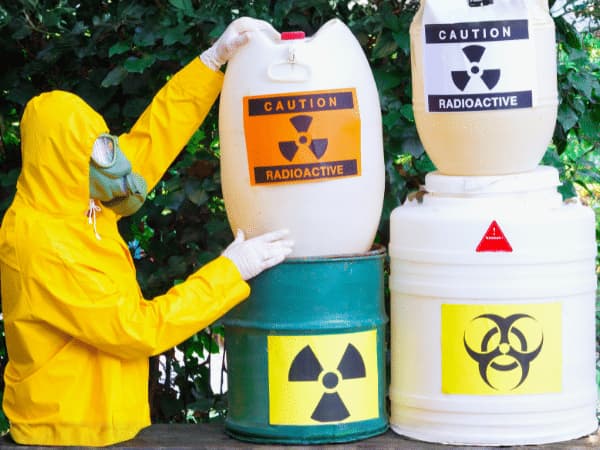 Contenitori di rifiuti pericolosi con etichette di rischio radioattivo e biologico gestiti da operatore protetto